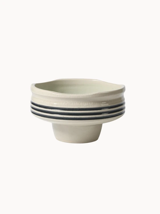 Ceramiczna miska na podwyższeniu w jasnokremowym kolorze, pokryta spękanym szkliwem z trzema czarnymi paskami wokół środka.