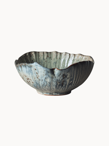 Rustykalna ceramiczna miska pokryta melanżowym jasnoniebieskim i beżowym szkliwem z brązowymi, nakrapianymi detalami na jednolitym białym tle.