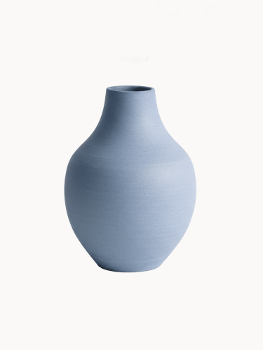 Ceramiczny wazon o matowym, teksturowanym wykończeniu w jasnoniebieskim kolorze na jednolitym białym tle. Ma kształt łzy z szerokim, zaokrąglonym korpusem, który zwęża się ku górze w krótką szyjkę.